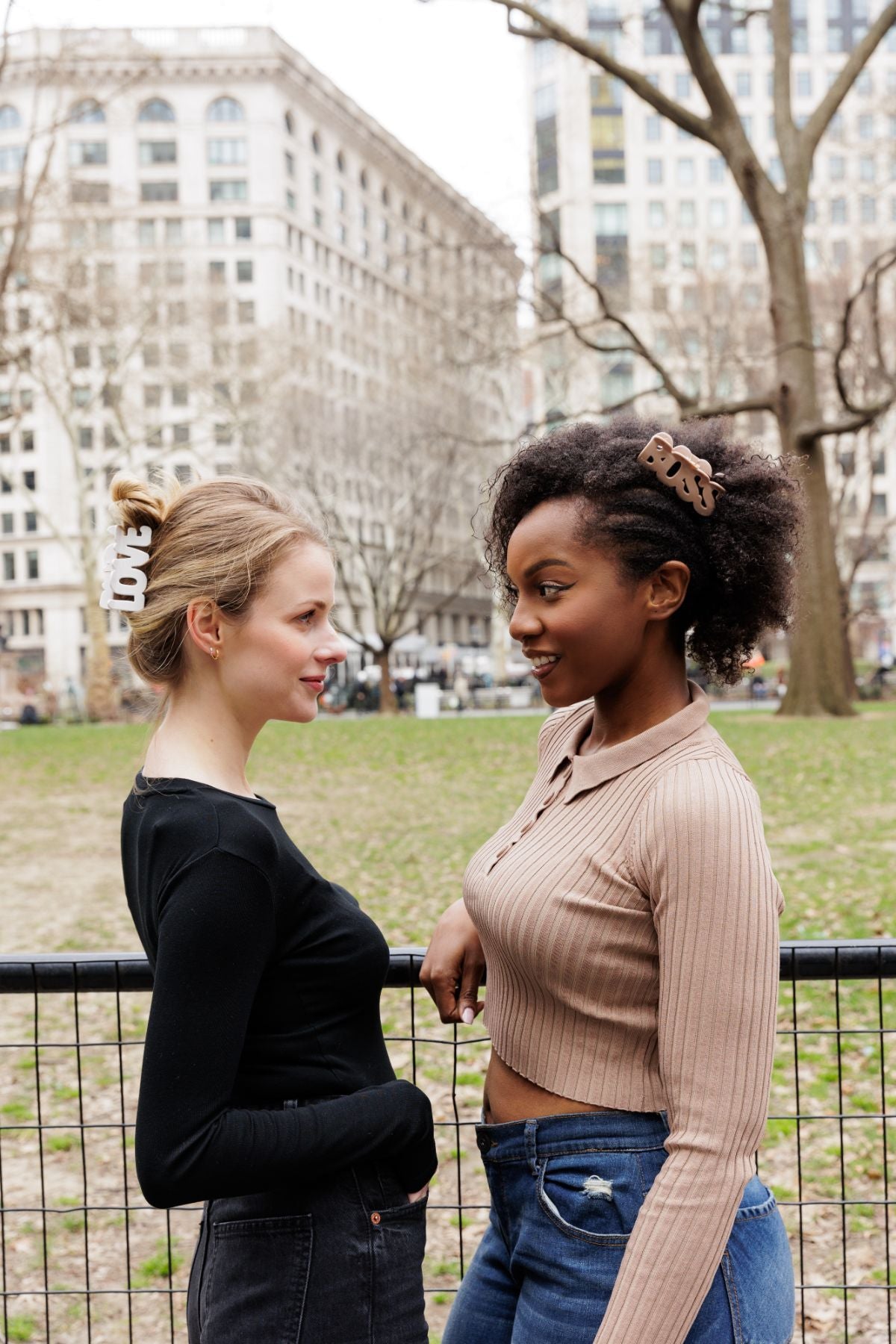 Two women speak with each other in NYC while wearing patented FiZZY hair clips for women that say "LOVE" and "BOSS"