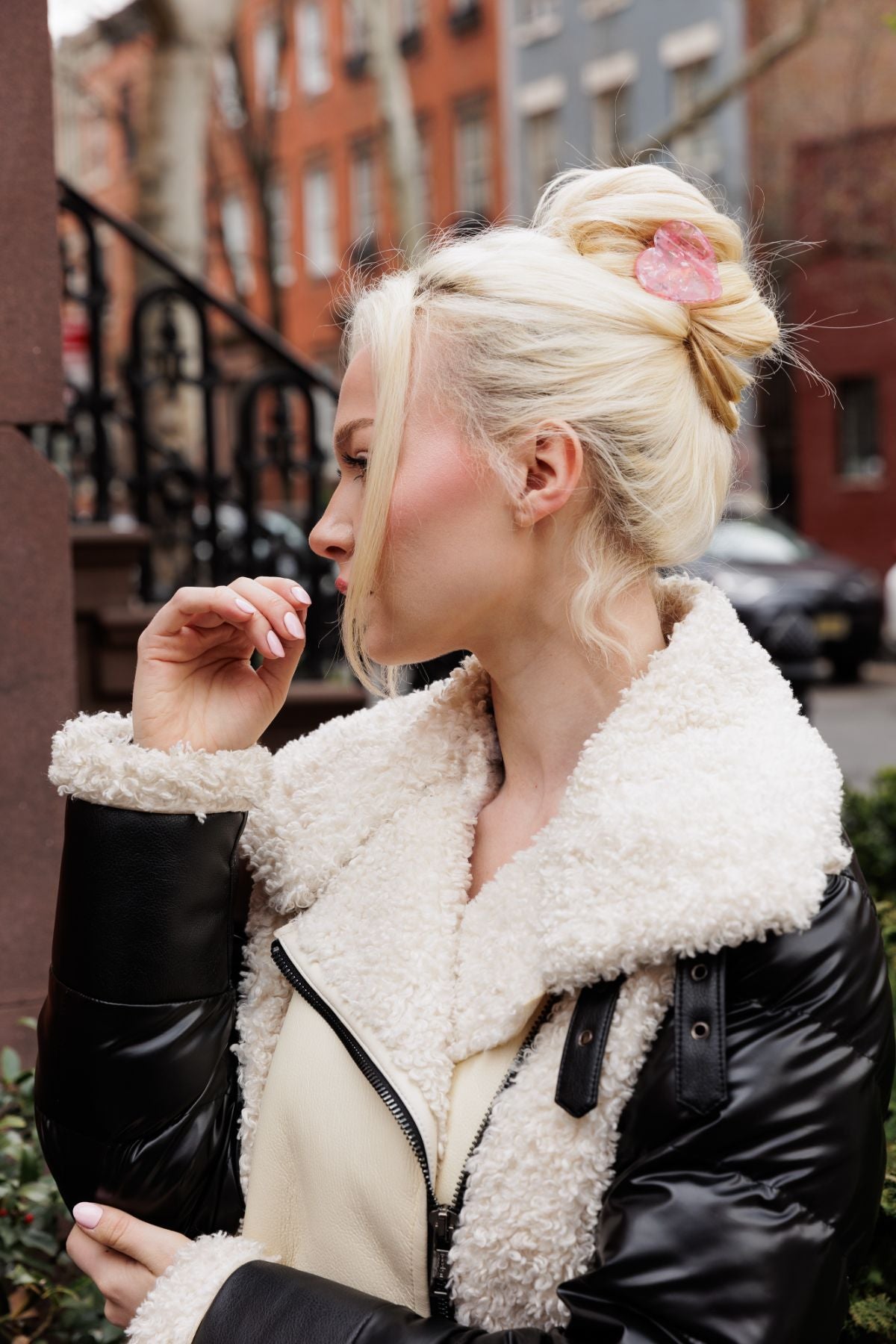 Blonde woman with black puffy jacket wears her hair styled in an updo using a FiZZY Original Heart Clippy in pink showcasing one of many available hair accessories for wholesale