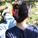 Person with a bun wearing an orange and blue collegiate Auburn hair clip outdoors